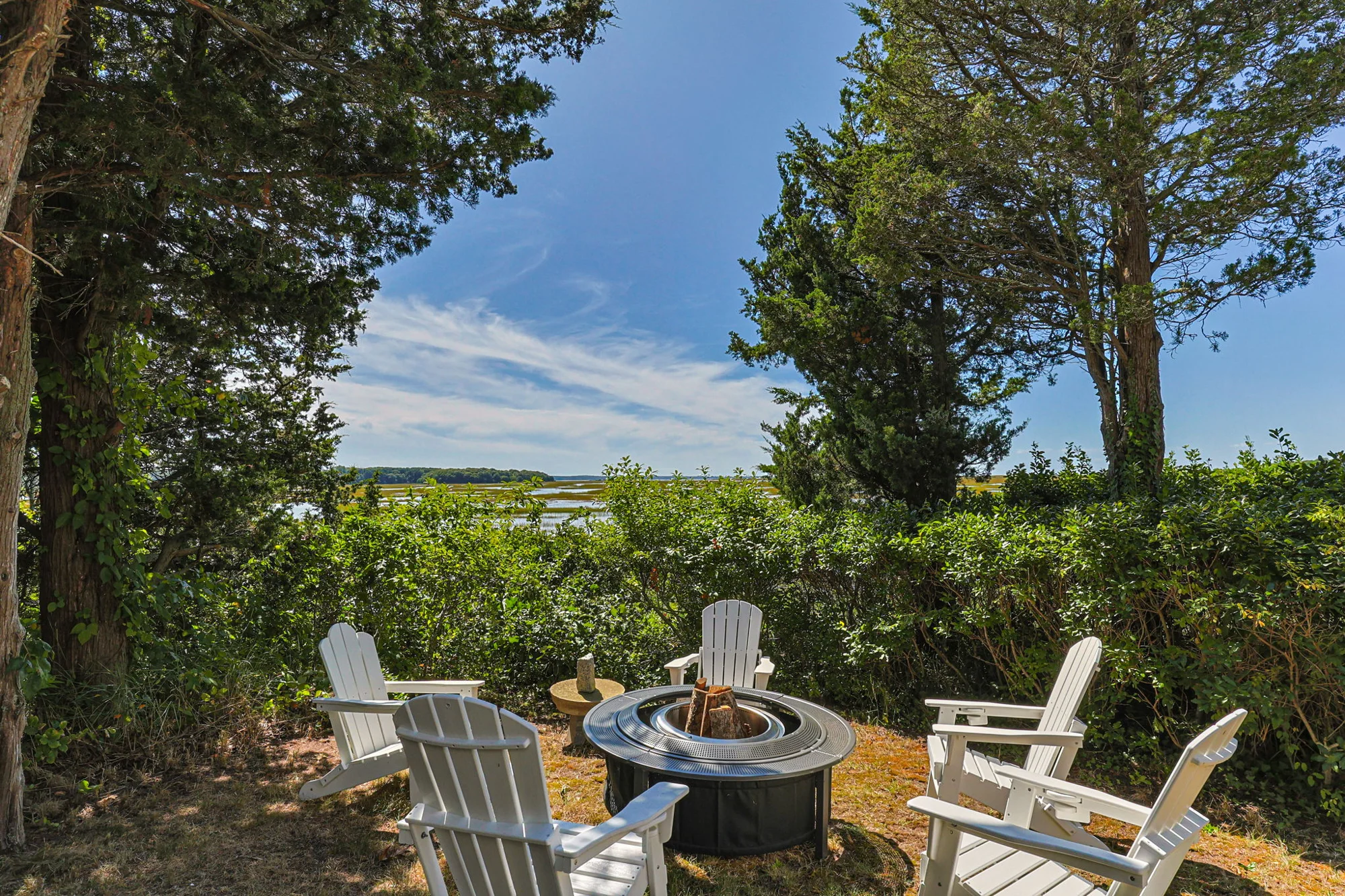 Adirondack chairs around a fire pit beside the marsh