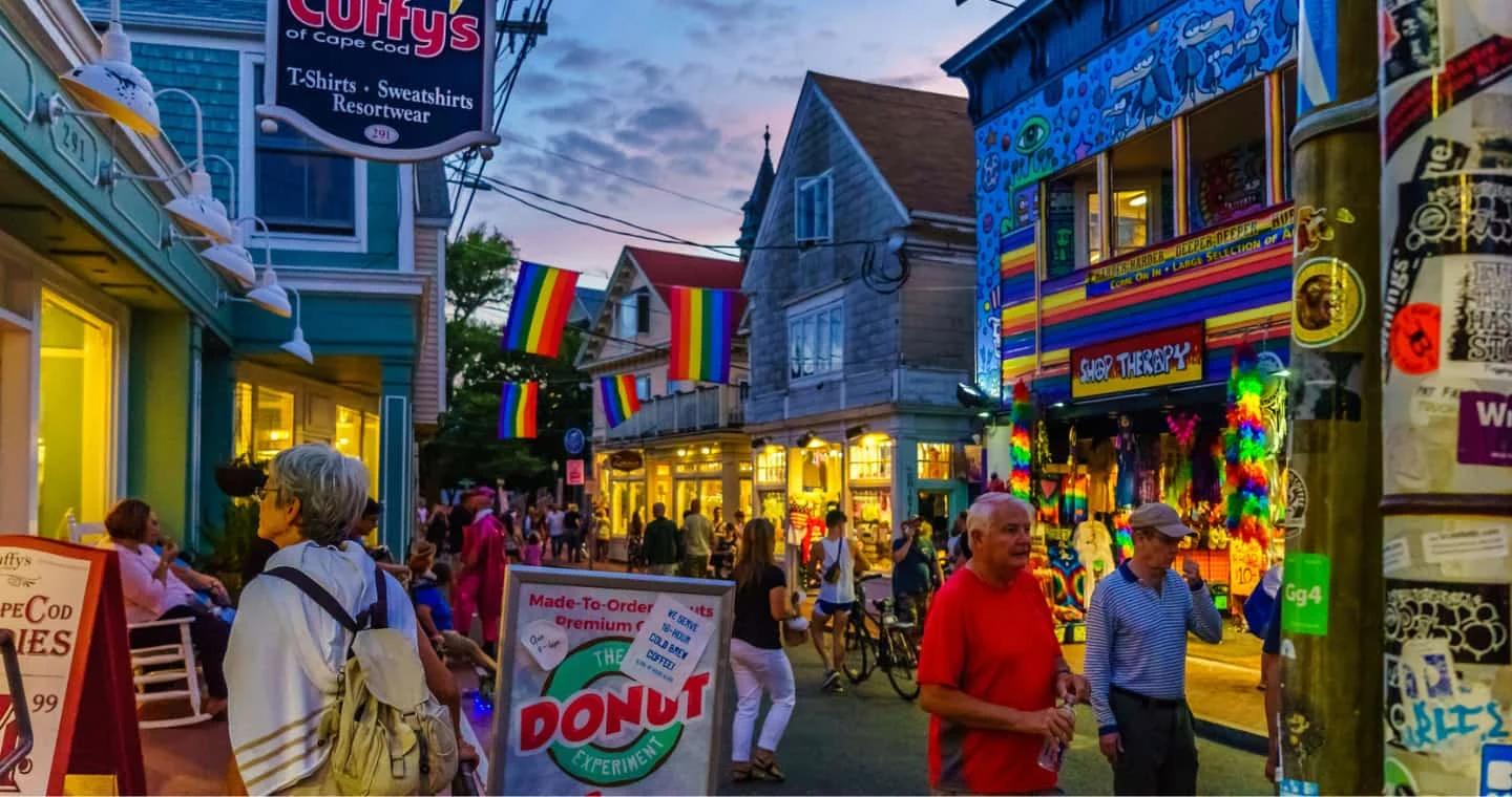 Shops, rainbow flags and pedestrians in Provincetown at dusk